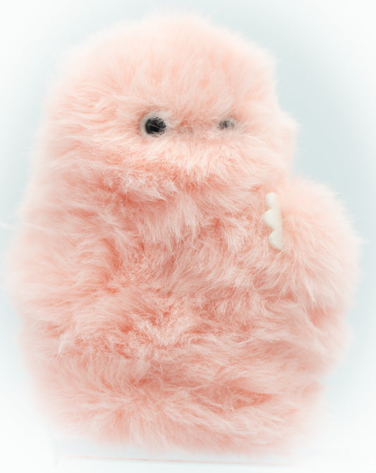 A fuzzy, fluffy pink robotic plush toy with small black eyes and a small white tooth, photographed against a soft light blue background.