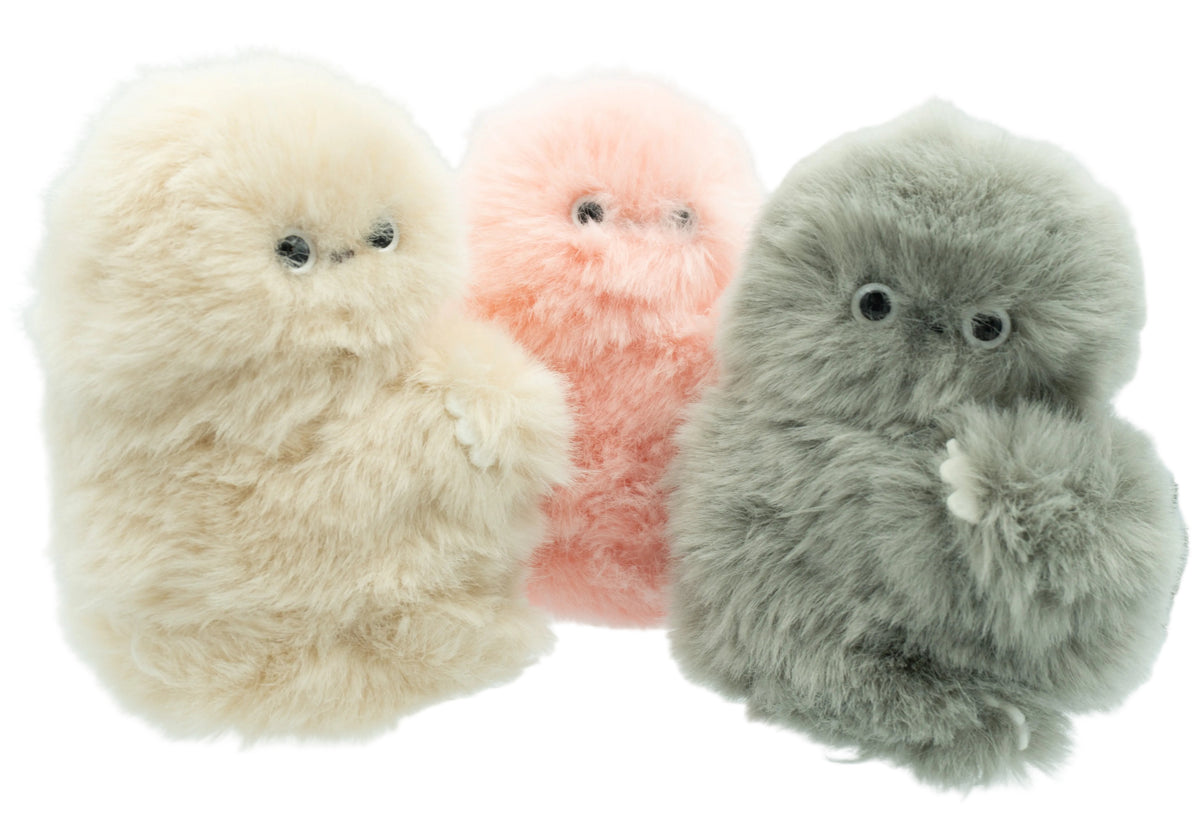 Three fluffy robot toy plushies in cream, pink, and gray, arranged side by side on a white surface against a light background.