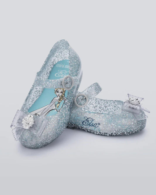Pair of glittery light blue children's Mary Jane shoes with Elsa character graphic, 'Elsa' text, and snowflake bows.
