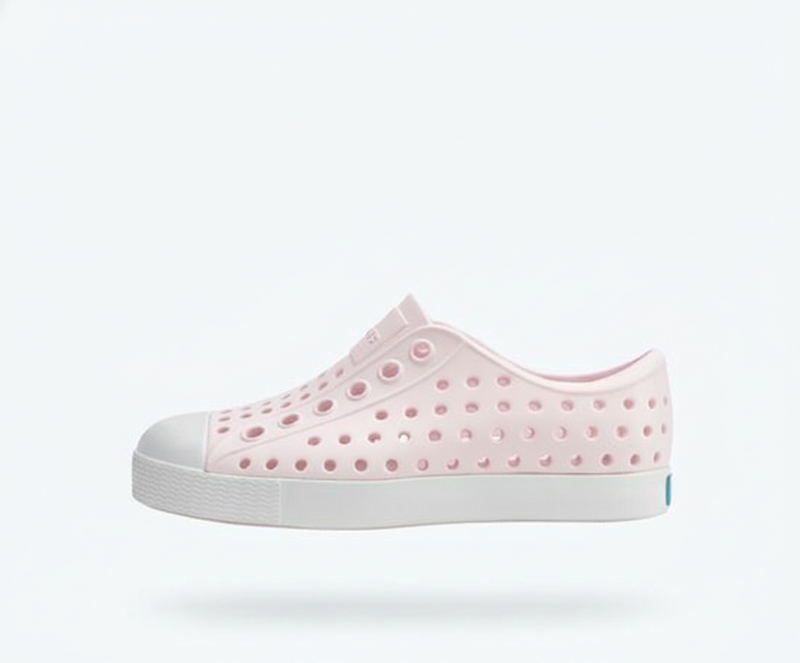 Light pink Native Jefferson kids' slip-on shoe with a perforated upper, white toe cap, and white sole, floating on a white background.