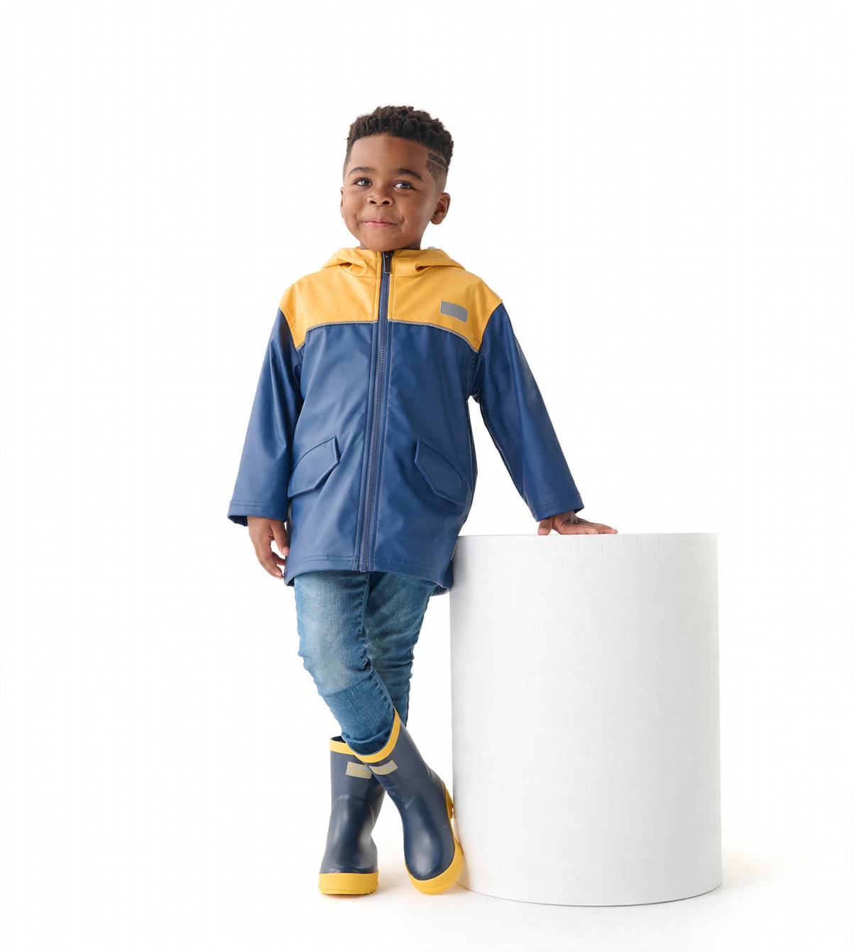 Yellow and navy zip-up rain jacket on a child, featuring a hood and front pockets, paired with blue jeans and rain boots.
