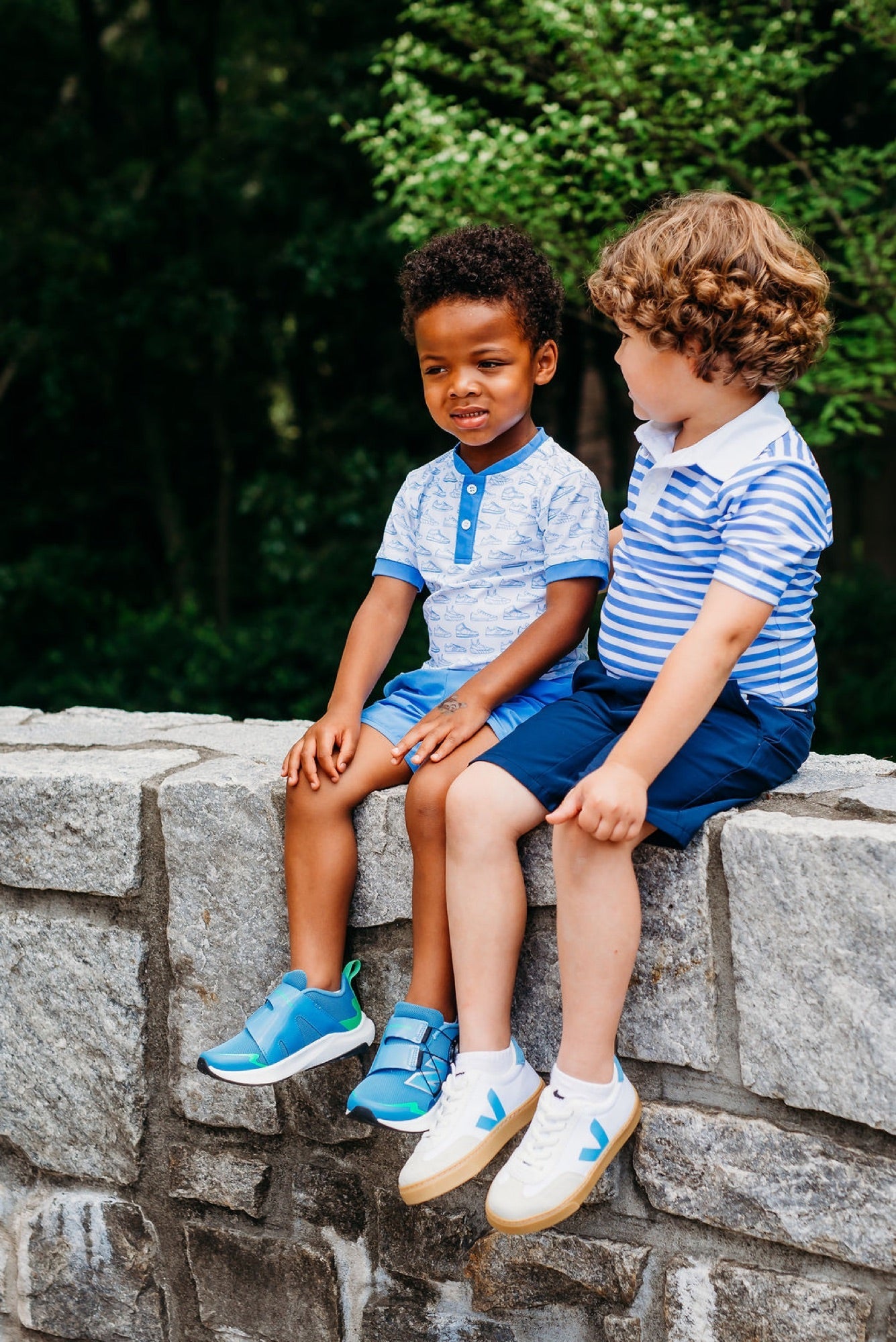 Two boys sitting on a stone wall wearing sneakers