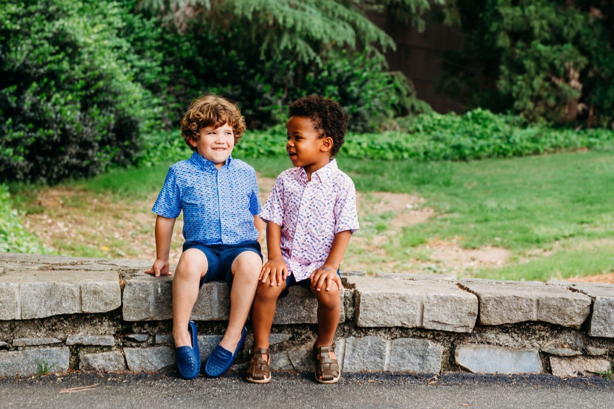 Two boys in button-downs sitting on a stone wall