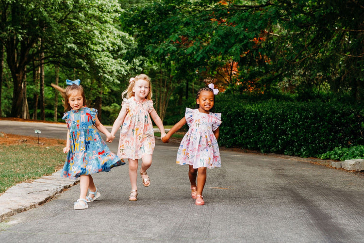Three girls running hand-in-hand in colorful print dresses