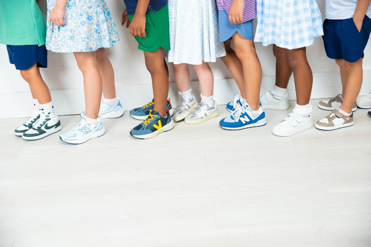 Row of children's sneakers and shoes lined up on a light wood floor