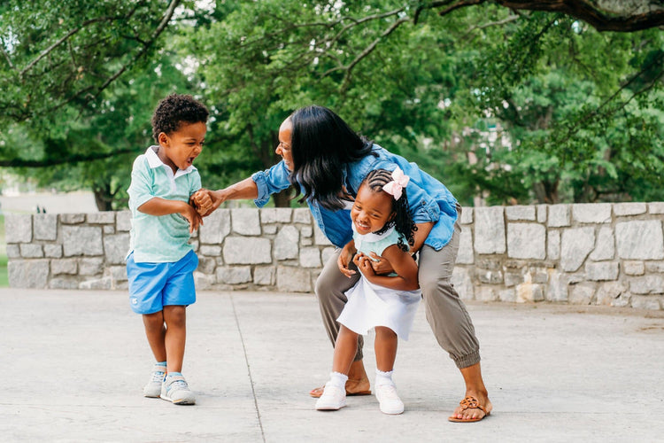 Parent playing outdoors with toddler and young child in shoes