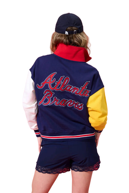 Person wearing a navy Atlanta Braves jacket with red and yellow accents on a red background