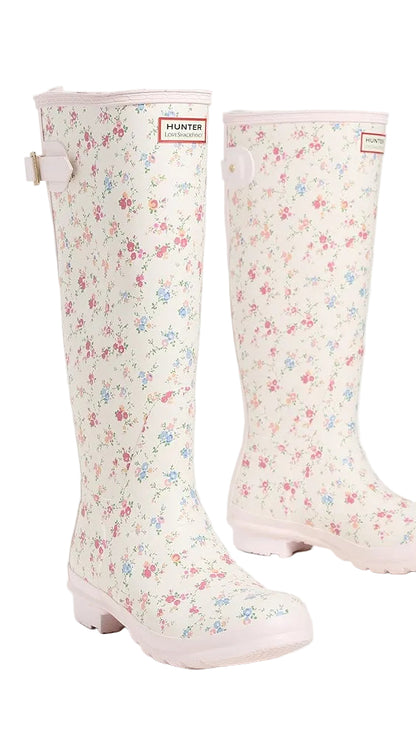 Tall rain boots with a cream base, small pink and blue floral print, pink sole, and a Hunter x LoveShackFancy logo patch.