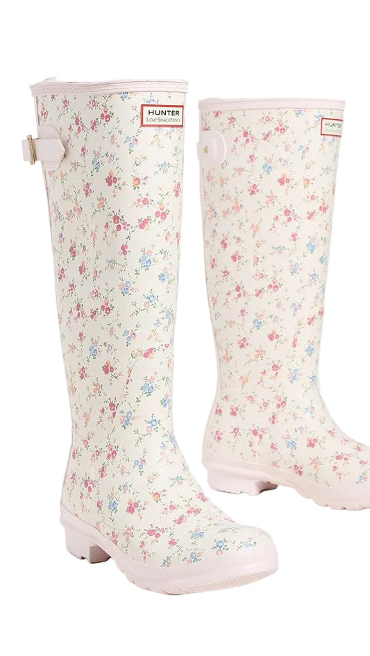 Hunter x LoveShackFancy tall cream rain boots with a delicate pink and blue floral pattern, light pink soles, and an adjustable buckle.