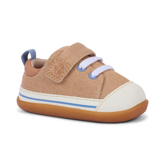 Tan children's sneaker with a white toe cap, white laces, blue eyelets, a Velcro strap with an embossed logo, and a blue and white striped sole.