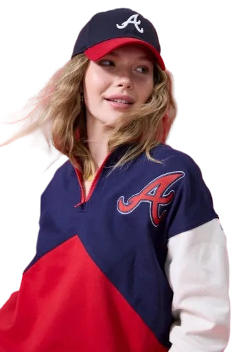 Smiling woman in a navy and red Braves baseball cap and a navy, red, and white colorblock quarter-zip sweatshirt with a red 'A' logo.