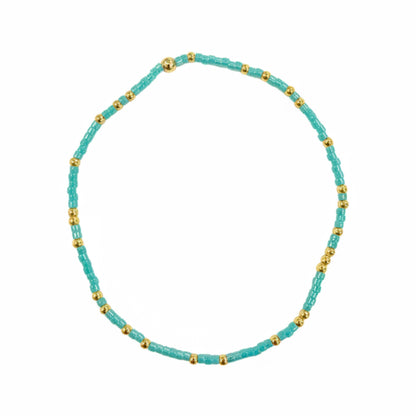 Turquoise beaded bracelet with small gold beads interspersed, forming a circular shape on a white background.