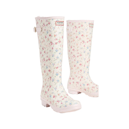 Tall rain boots with a cream base, small pink and blue floral print, pink sole, and a Hunter x LoveShackFancy logo patch.
