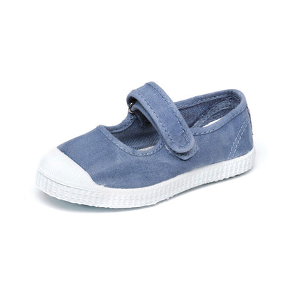 Blue canvas children's Mary Jane shoe with a white rubber toe cap and sole, featuring a Velcro strap and white stitching.