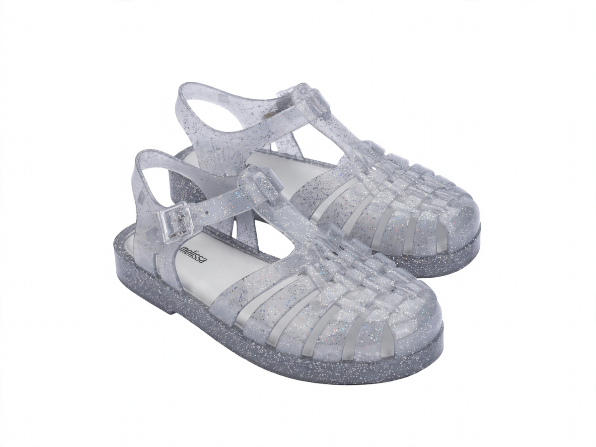 Pair of clear glitter Mini Melissa jelly sandals with a caged toe, ankle strap, and flat sole.