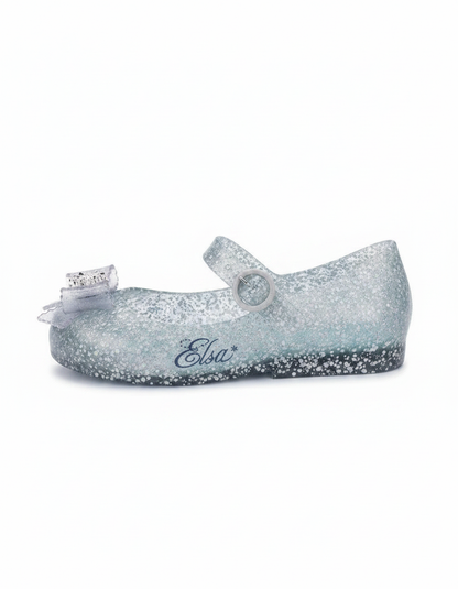 Glittery translucent light blue Mary Jane flat with a clear bow on the toe, a buckle strap, and 'Elsa*' written on the side.