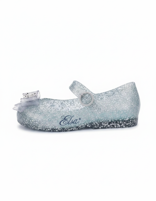 Glittery translucent light blue Mary Jane flat with a clear bow on the toe, a buckle strap, and 'Elsa*' written on the side.