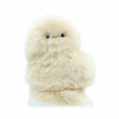 A fluffy cream-colored robotic plush toy with large black eyes and a small stitched nose, standing upright on a clear display base against a light blue background.