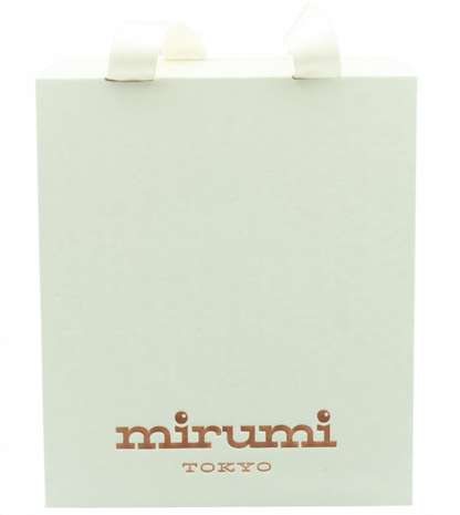 A cream-colored paper gift bag with white ribbon handles and the brand name 'mirumi TOKYO' printed in brown at the bottom, set against a light blue gradient background.