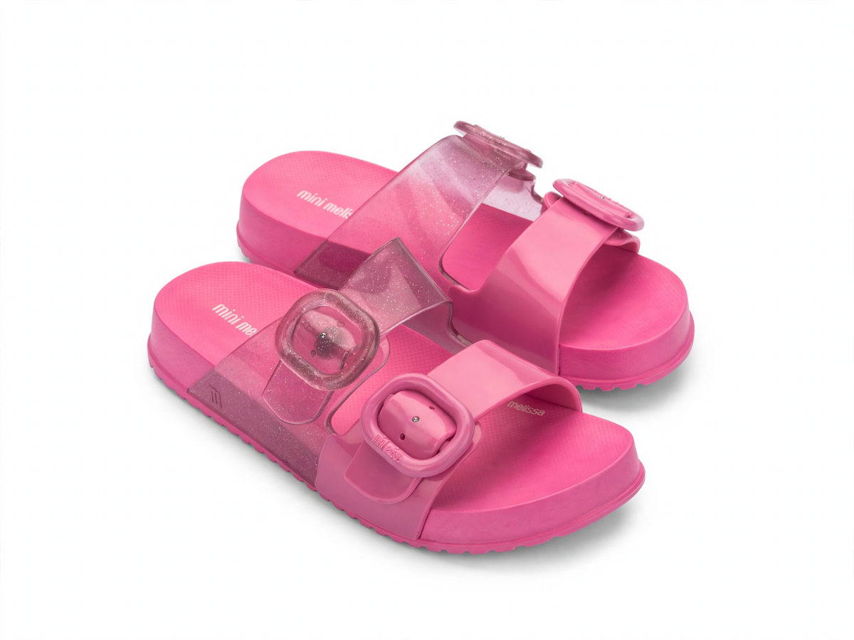 Pair of hot pink Mini Melissa Cozy Slide sandals featuring clear glitter straps with buckle details and a textured footbed.