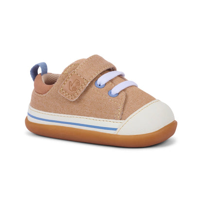 Tan canvas baby sneaker with white toe cap, white laces, blue eyelets and stripe, a velcro strap, and a brown rubber sole.