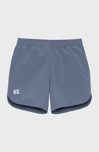 Children's slate blue athletic shorts with an elastic waistband, a white K logo on the left leg, and curved hems.